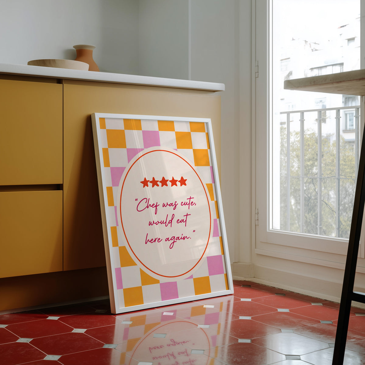Chef Was Cute print in a white frame against yellow cabinets on a red tiled floor