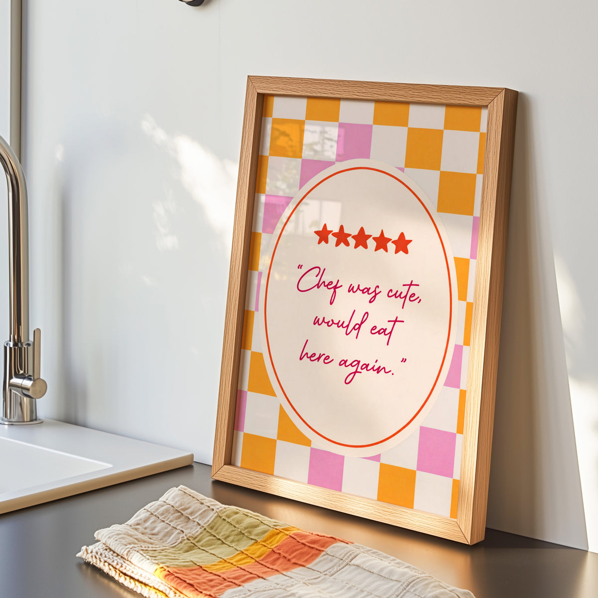 Chef Was Cute print in an oak frame by the kitchen sink beside a striped tea towel