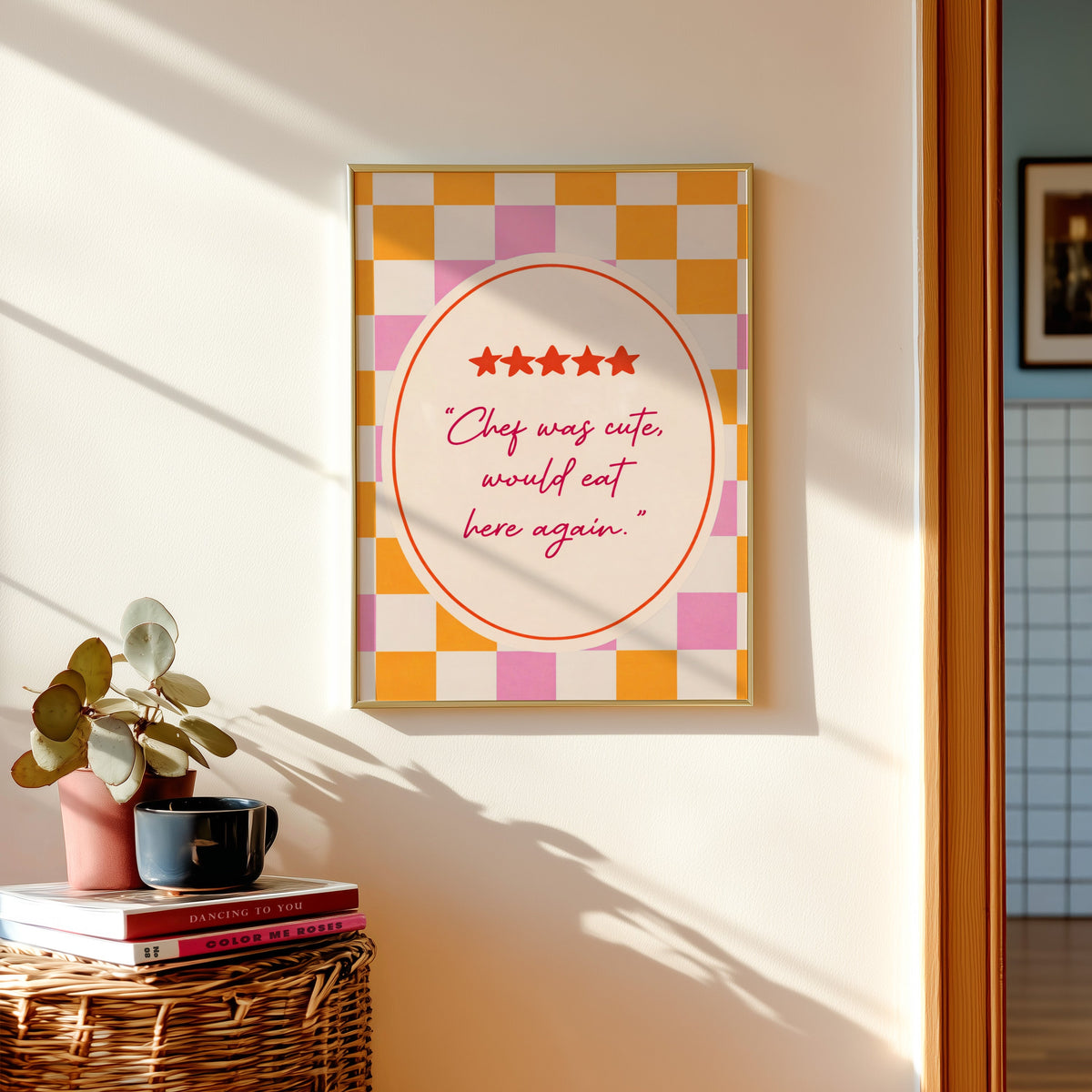 Chef Was Cute print shown in a gold frame above a basket of books and a pilea plant