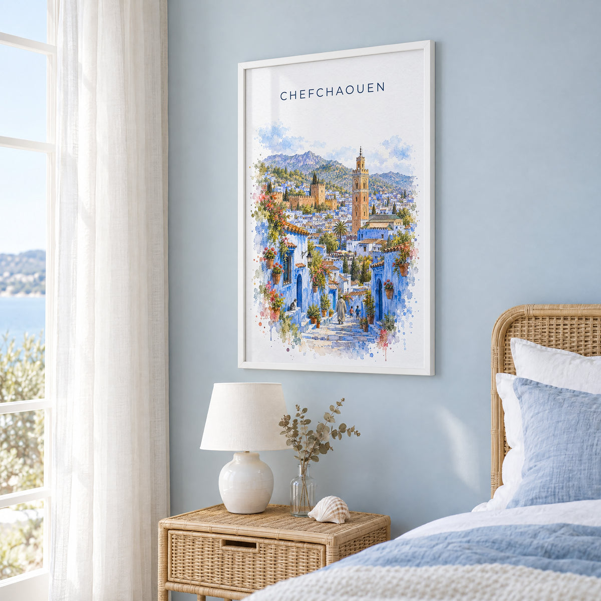 Chefchaouen watercolor print in a white frame on a pale blue wall beside a rattan bed in a coastal bedroom