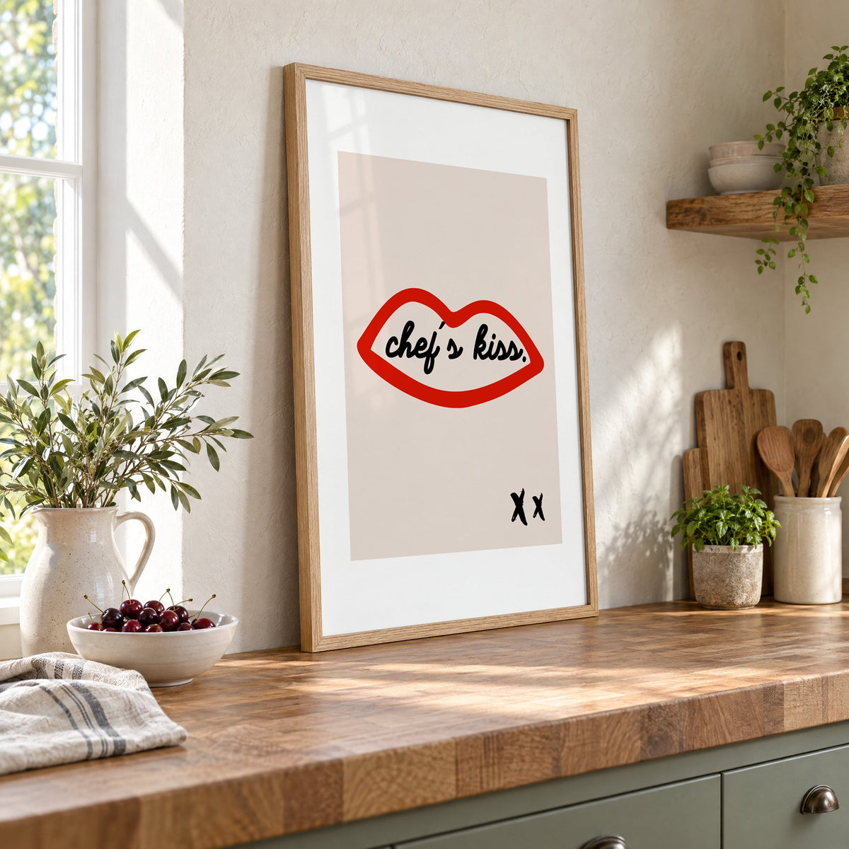 Chef's kiss red lips outline print in an oak frame leaning on a butcher block island beside a bowl of cherries