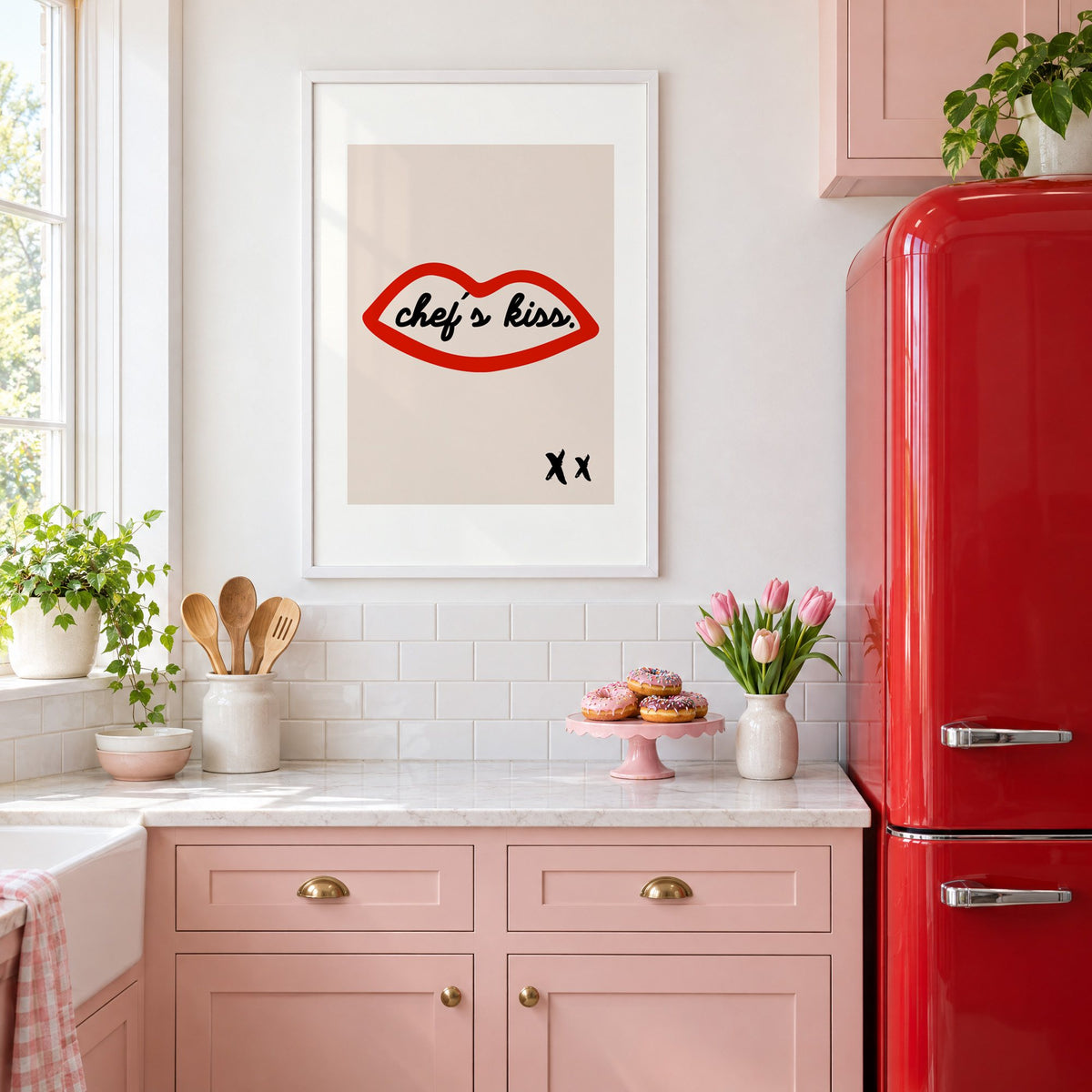 Chef's kiss red lips outline print in a white frame in a pink kitchen beside a red retro fridge