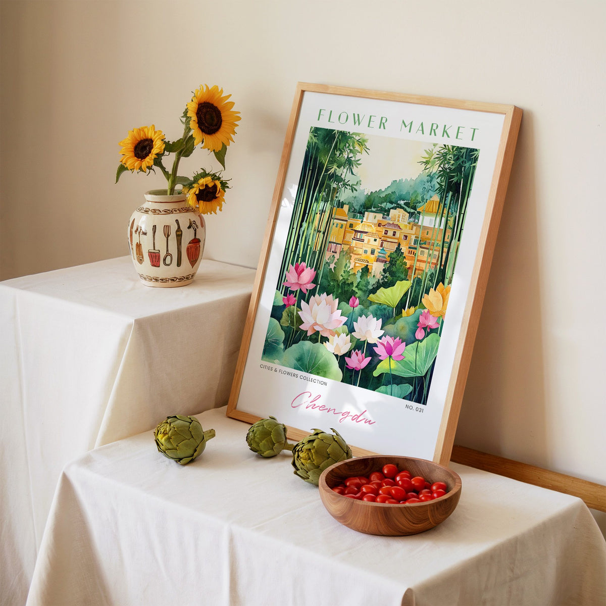 Chengdu flower market print in an oak frame leaning on a linen-draped table beside a vase of sunflowers