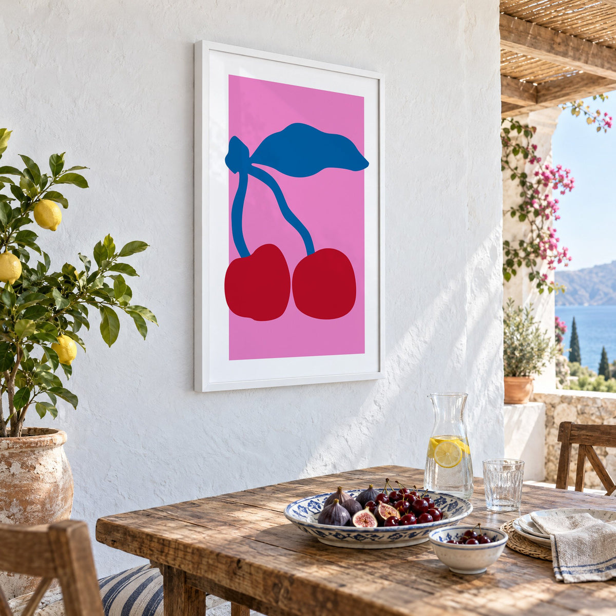 giant red cherries cobalt leaf hot pink print in a white frame on a whitewashed terrace wall above a lunch table with figs and cherries, seen at an angle