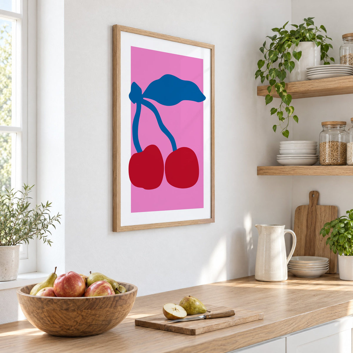 giant red cherries cobalt leaf hot pink print in an oak frame on a white kitchen wall above a counter with apples and pears, seen at an angle