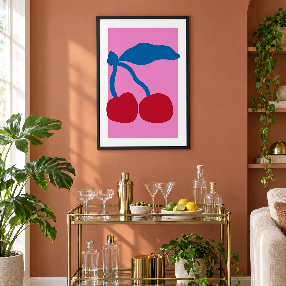 giant red cherries cobalt leaf hot pink print in a black frame on a terracotta wall above a brass bar cart with coupes and citrus