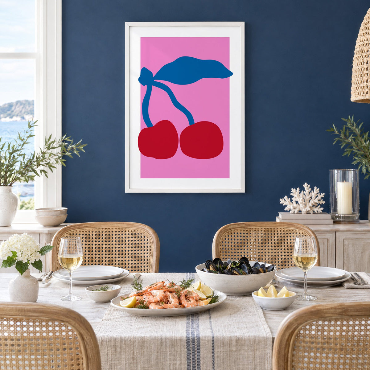 giant red cherries cobalt leaf hot pink print in a white frame on a navy wall above a dining table set with shrimp and mussels