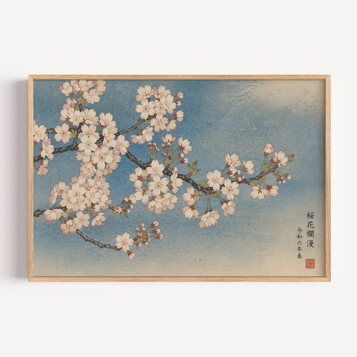 Cherry blossom branch on a blue sky print in a light oak frame on a plain white wall