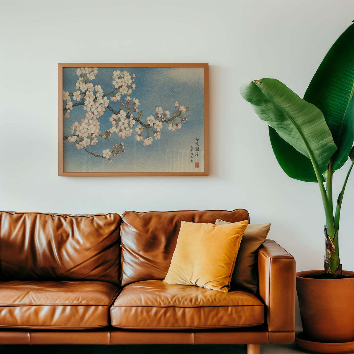 Cherry blossom branch on a blue sky print in a warm oak frame above a cognac leather sofa with a mustard pillow