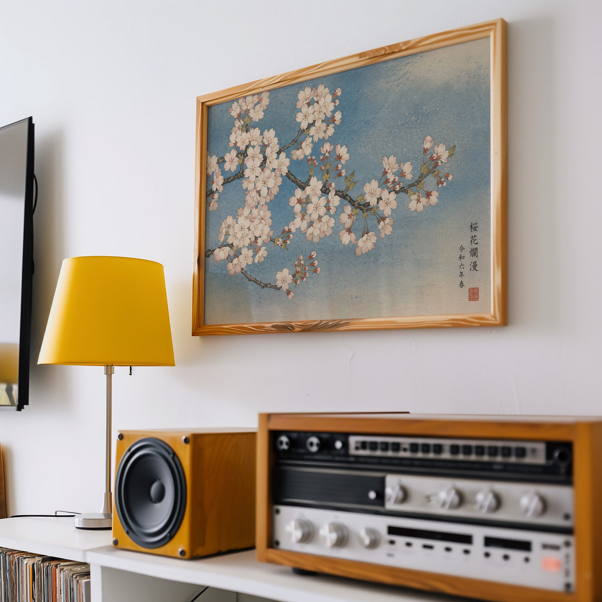 Cherry blossom branch on a blue sky print in a pine frame above a vintage stereo and a yellow table lamp