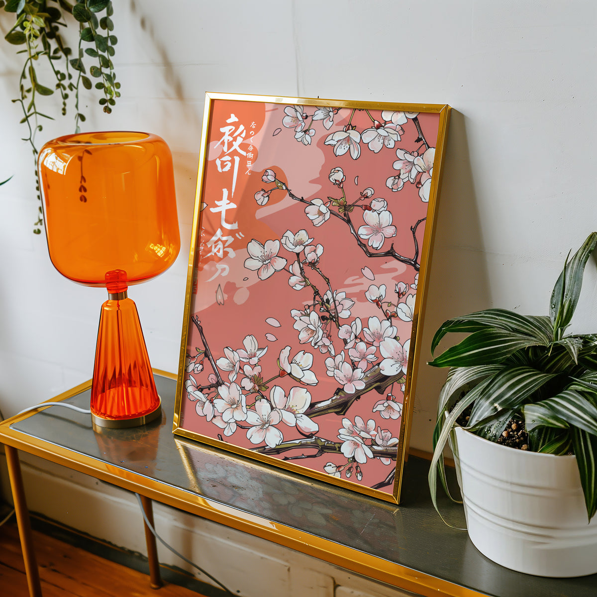 Cherry blossom branch on coral print shown in a gold frame on a console beside an orange glass lamp
