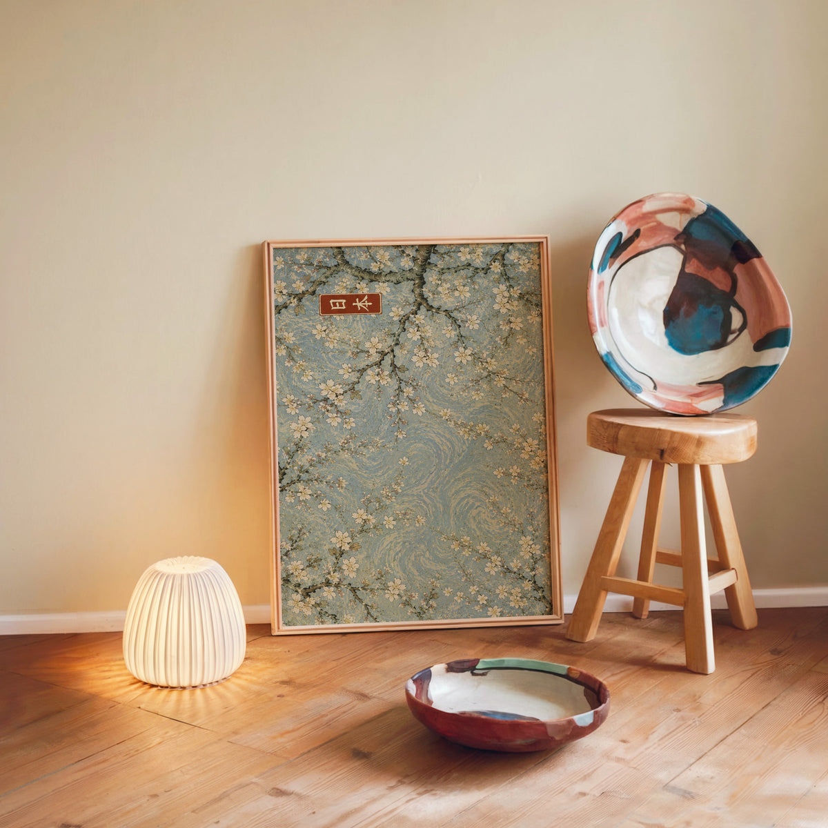 Cherry blossoms blue sky poster in a light wood frame leaning on a wooden floor by a glowing lamp and stool