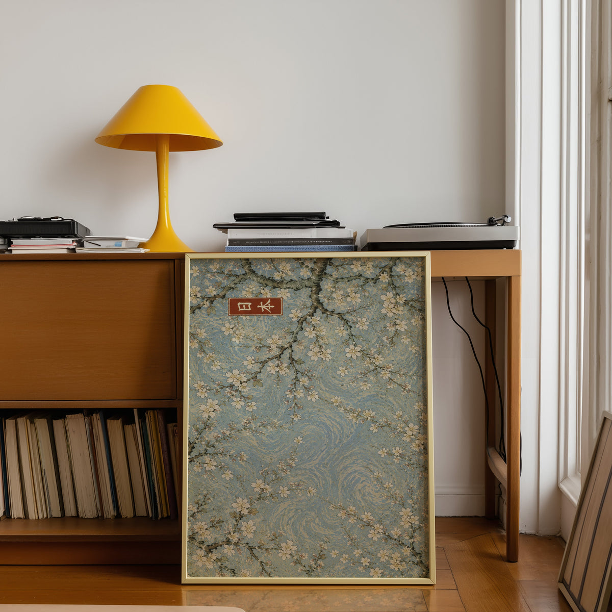 Cherry blossoms blue sky poster shown in a gold frame leaning under a teak desk with a yellow lamp