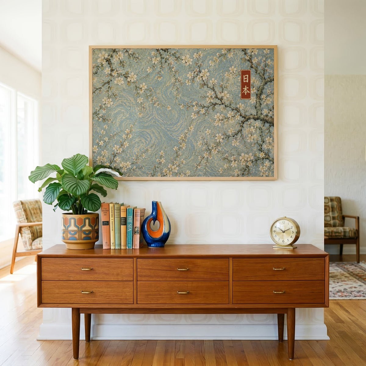 Cherry blossoms on a blue swirl sky print in a light oak frame above a teak credenza with books and a brass clock