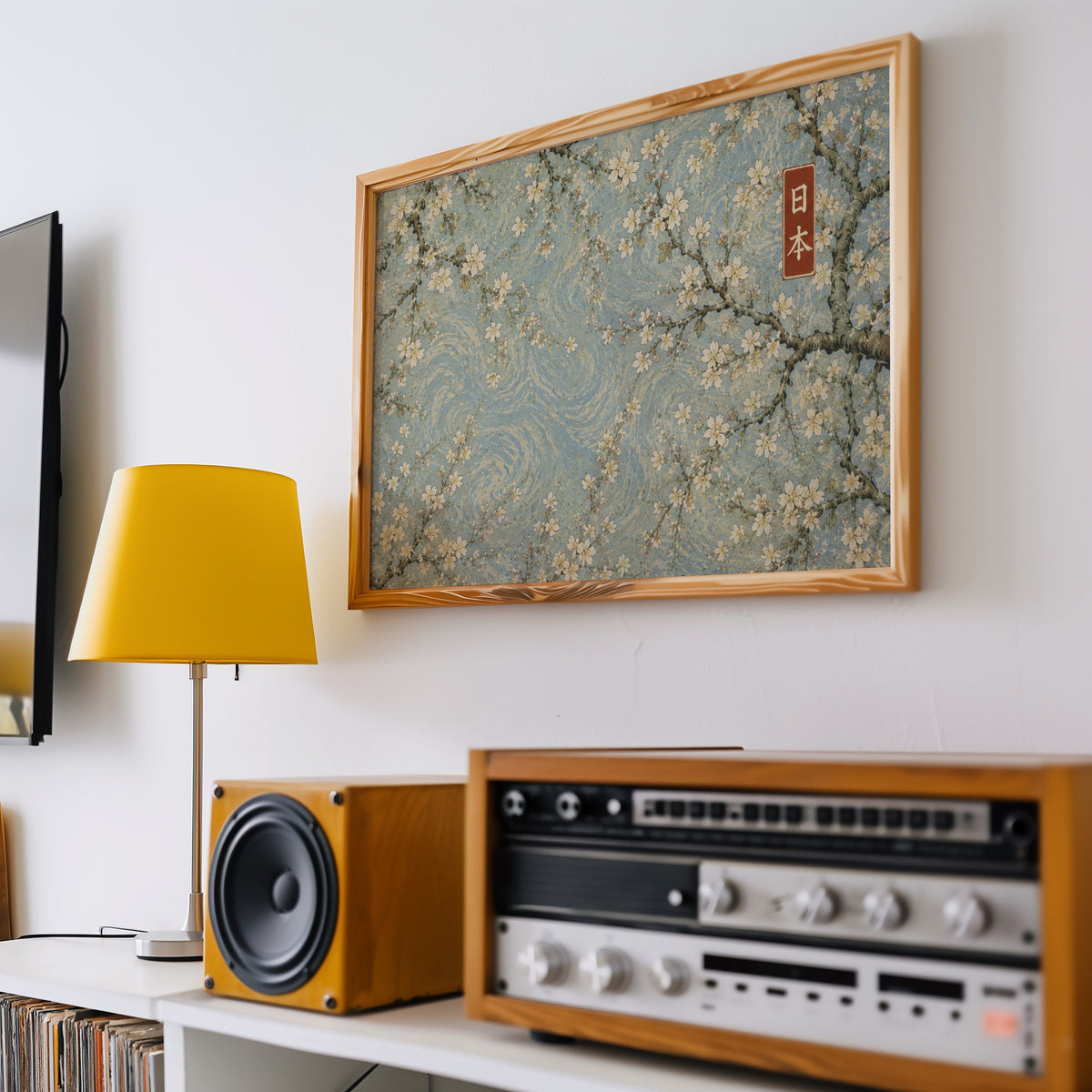 Cherry blossoms on a blue swirl sky print in a pine frame above a vintage stereo and a yellow table lamp