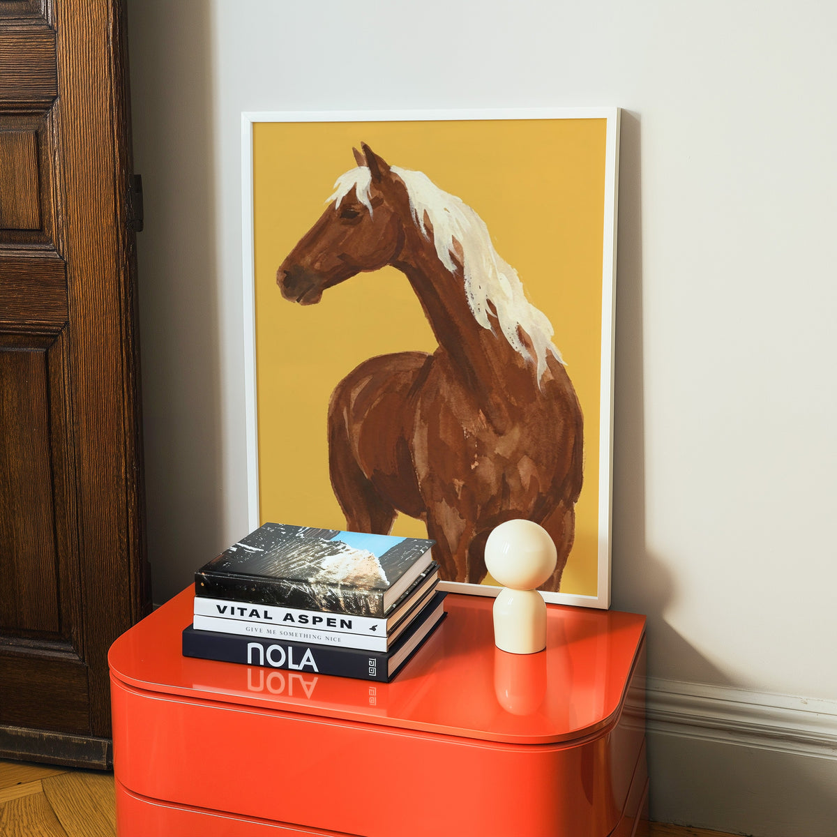 Horse with flaxen mane print in a white frame on a glossy orange cabinet with books