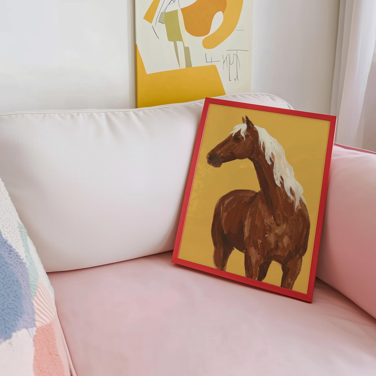 Brown horse wall art print shown in a red frame leaning on a blush pink sofa