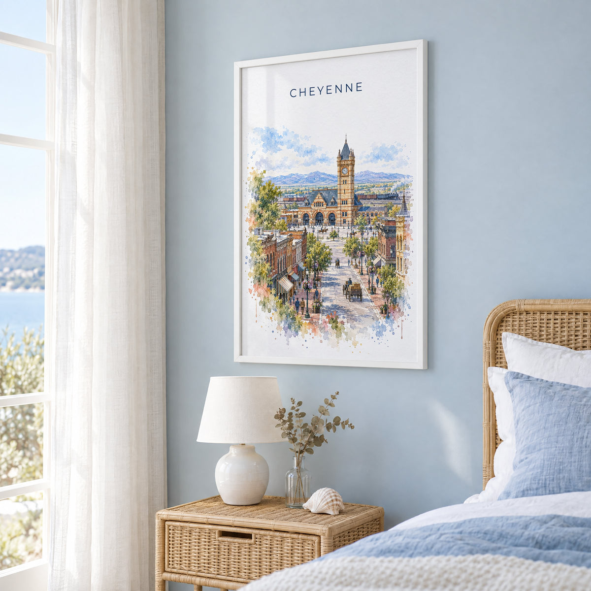 Cheyenne watercolor print in a white frame on a pale blue wall beside a rattan bed in a coastal bedroom