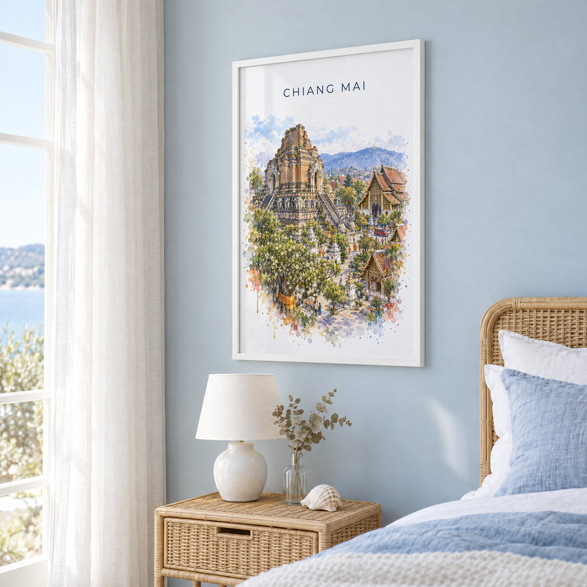 Chiang Mai watercolor print in a white frame on a pale blue wall beside a rattan bed in a coastal bedroom