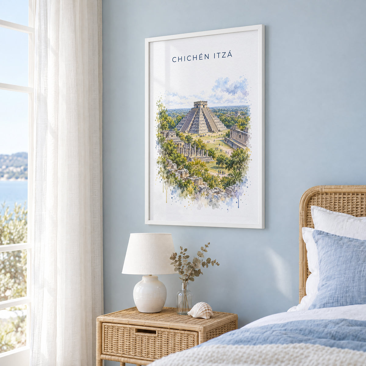 Chichen Itza watercolor print in a white frame on a pale blue wall beside a rattan bed in a coastal bedroom