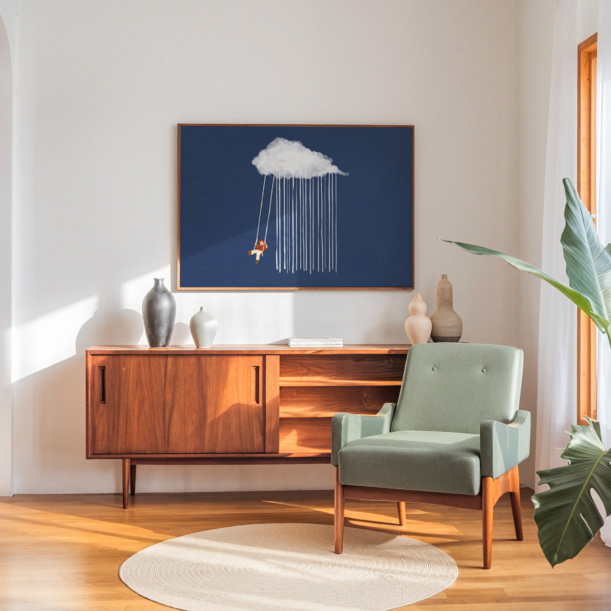 Surreal swing and rain print in a walnut frame above a sideboard beside a sage armchair