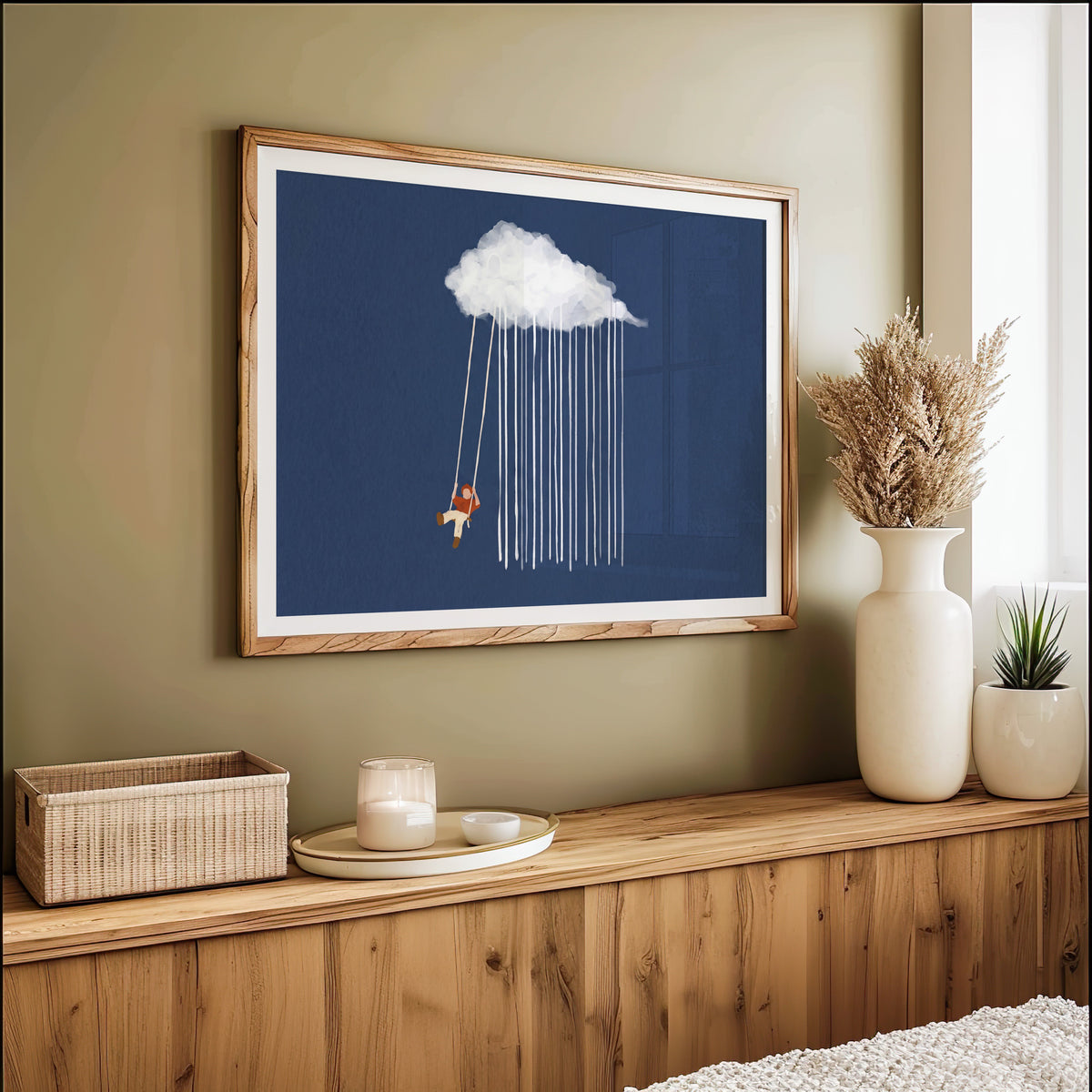 Child on a rain cloud swing print in an oak frame on an olive green wall above pampas grass
