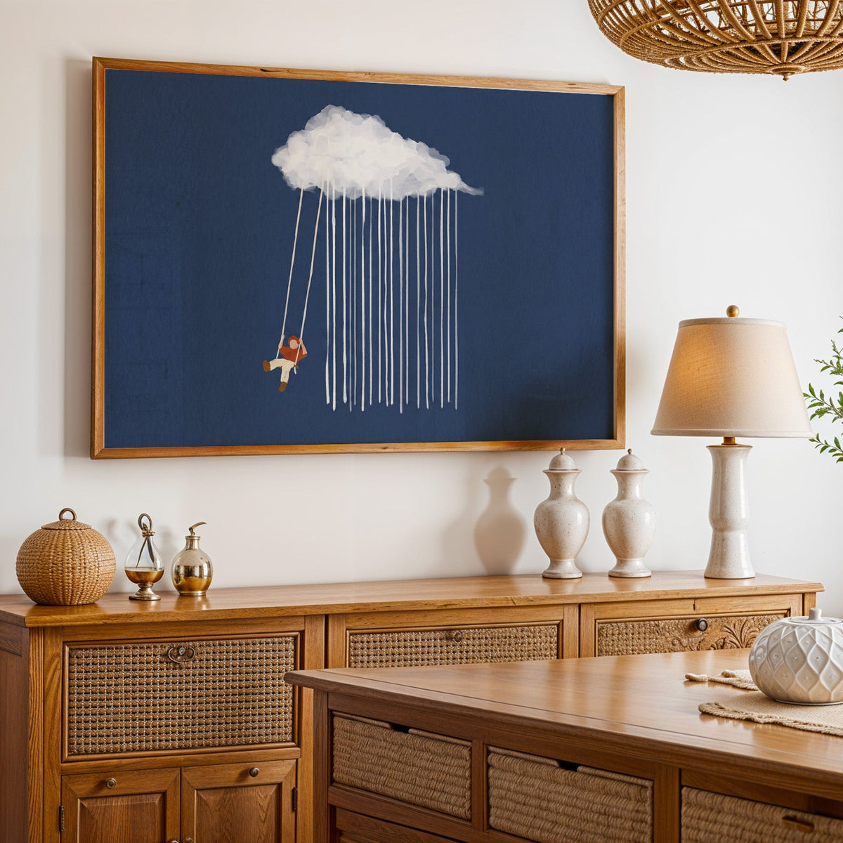 Whimsical rain cloud print in an oak frame above a cane sideboard with a table lamp
