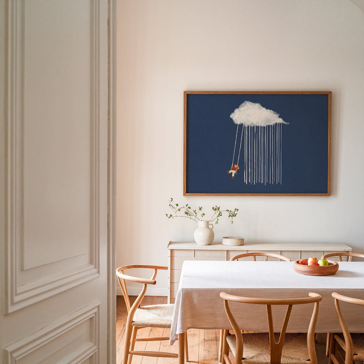 Blue rain cloud wall art print in an oak frame in a dining room with wishbone chairs