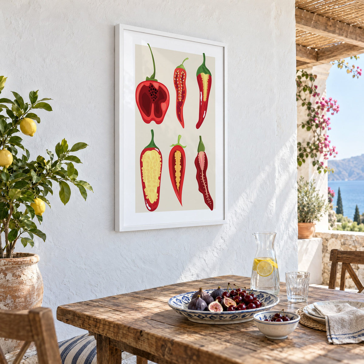 six sliced chili pepper cross sections print in a white frame on a whitewashed terrace wall above a lunch table with figs and cherries, seen at an angle