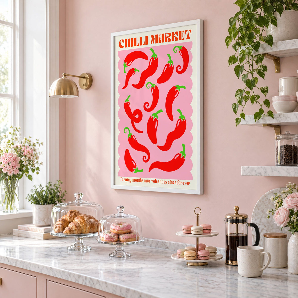 CHILLI MARKET red peppers pink scallop print in a white frame on a blush pink wall above a patisserie counter with croissants and macarons, seen at an angle