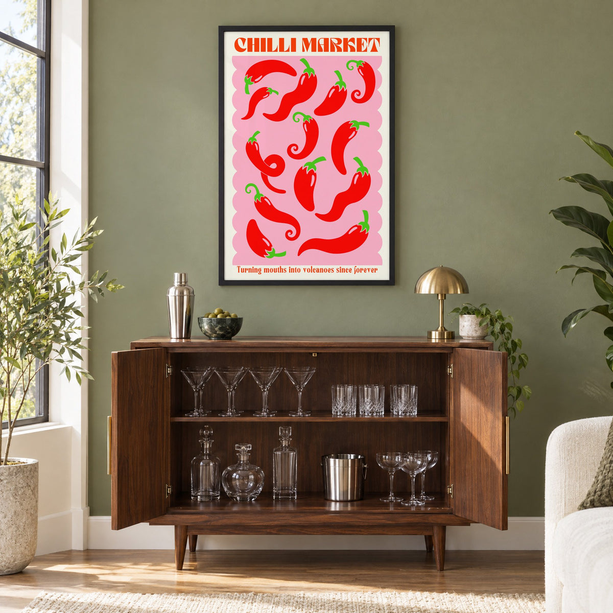 CHILLI MARKET red peppers pink scallop print in a black frame on an olive green wall above a walnut bar cabinet with glassware