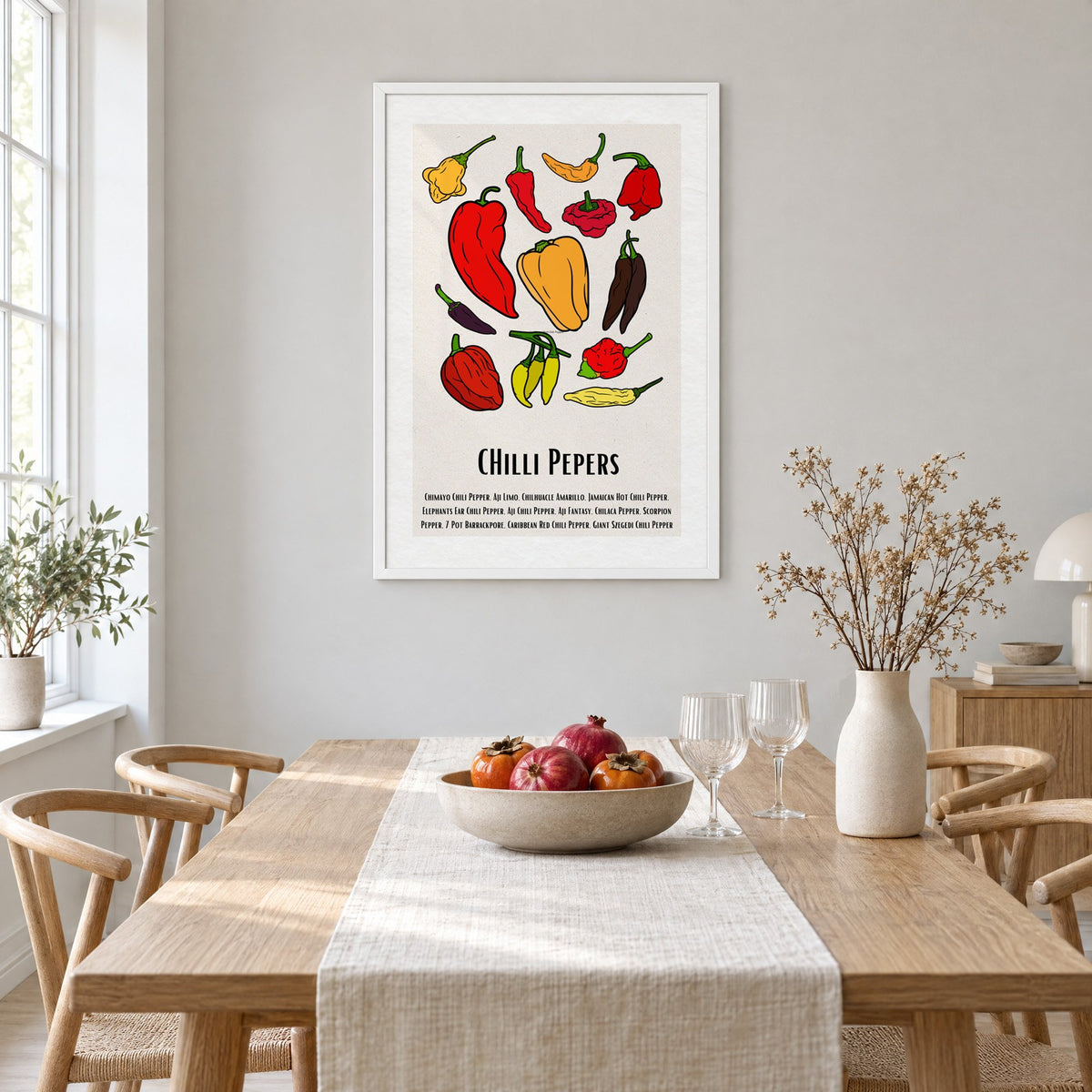 CHilli Pepers bold outline pepper chart print in a white frame above a light oak dining table with a linen runner and fruit bowl