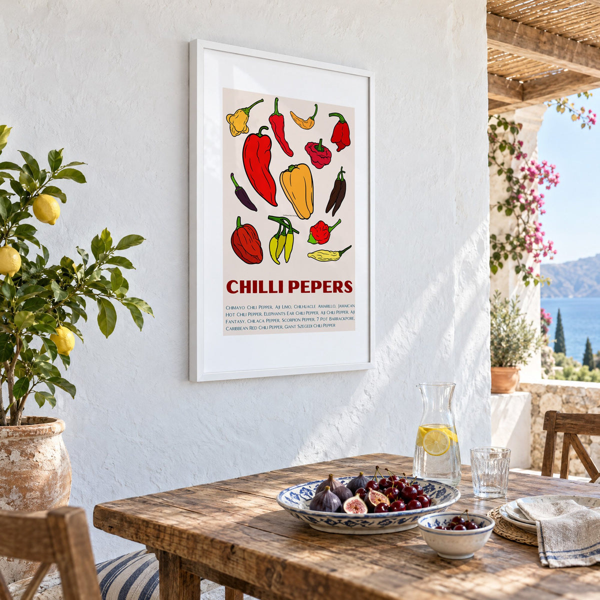 CHILLI PEPERS thirteen pepper chart print in a white frame on a whitewashed terrace wall above a lunch table with figs and cherries, seen at an angle