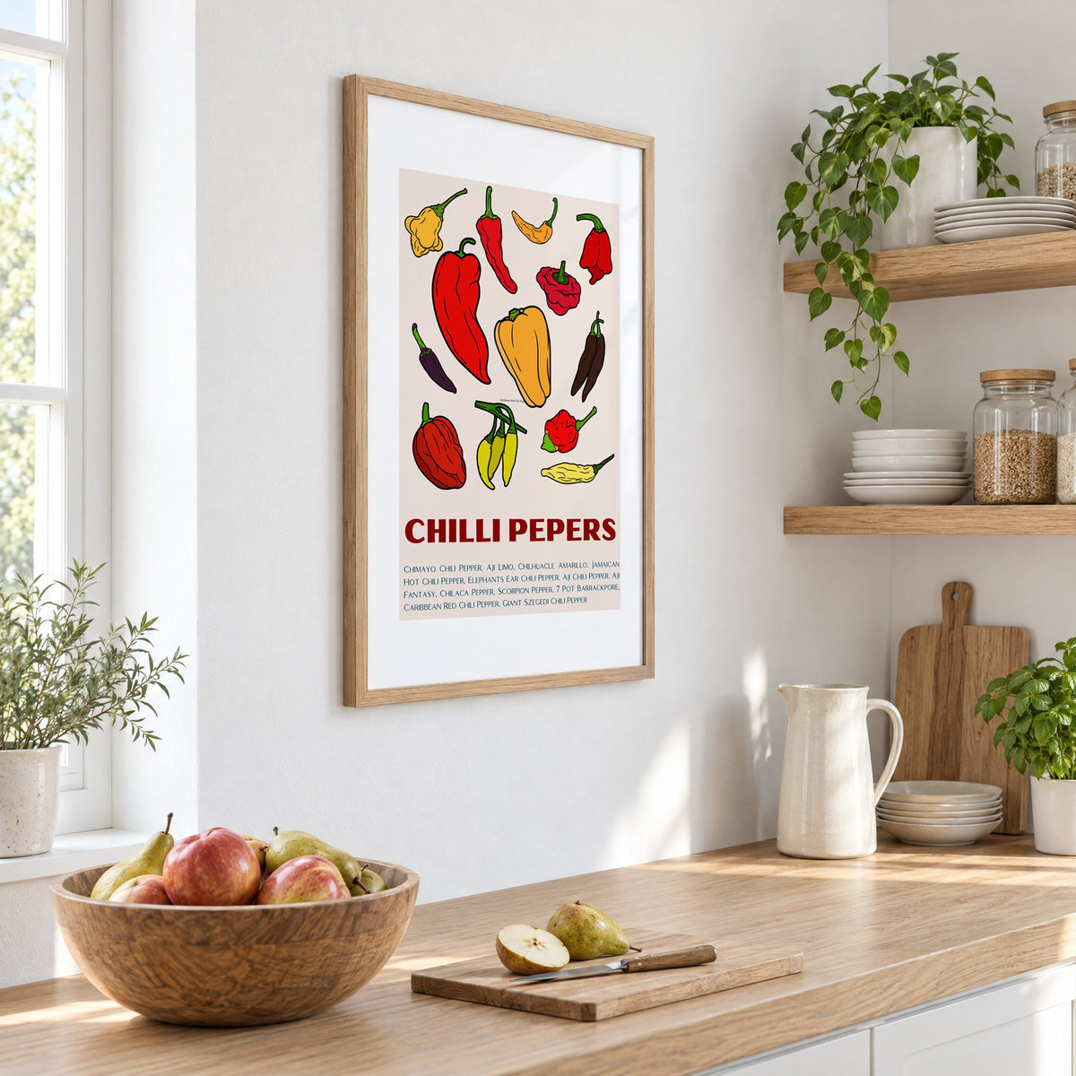 CHILLI PEPERS thirteen pepper chart print in an oak frame on a white kitchen wall above a counter with apples and pears, seen at an angle