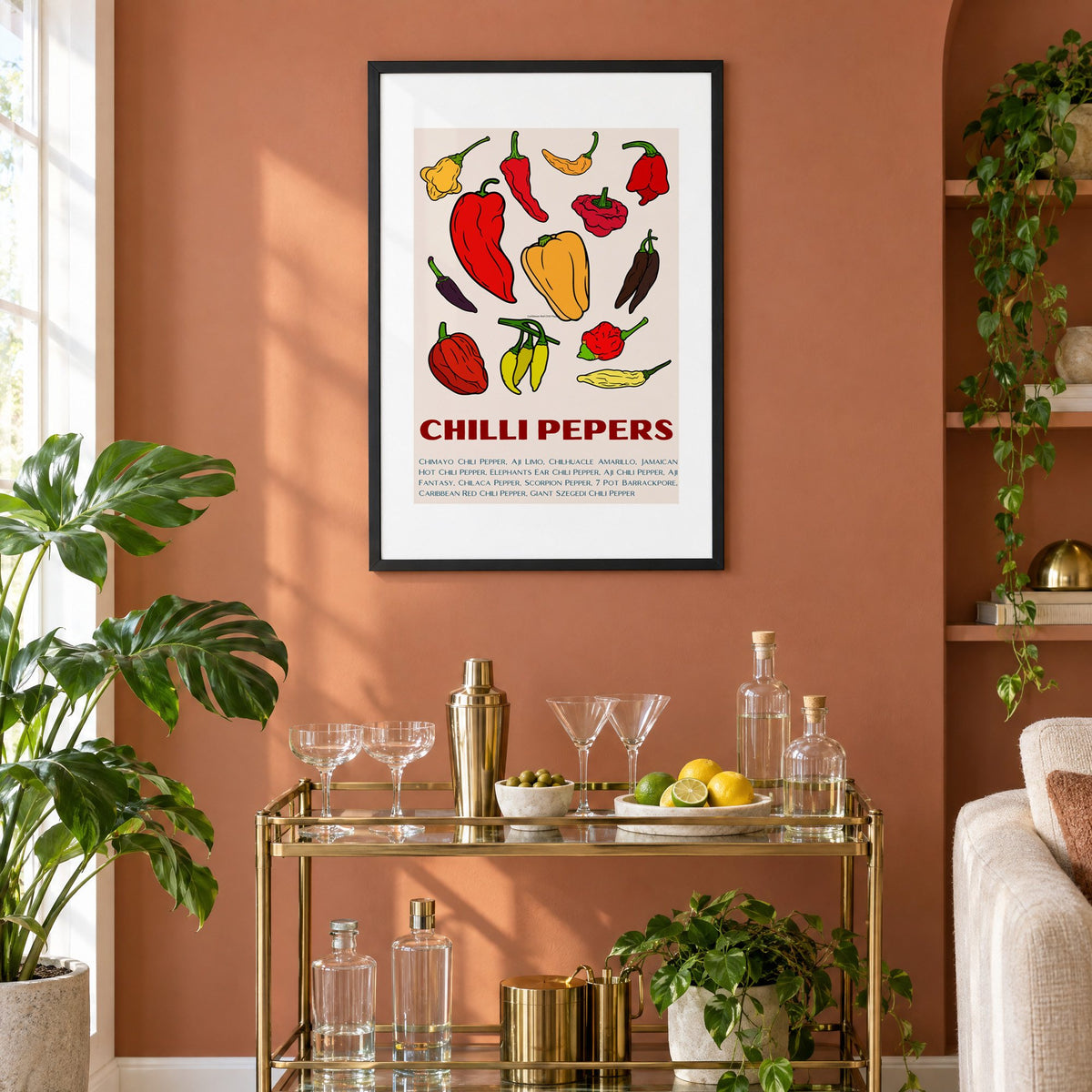 CHILLI PEPERS thirteen pepper chart print in a black frame on a terracotta wall above a brass bar cart with coupes and citrus