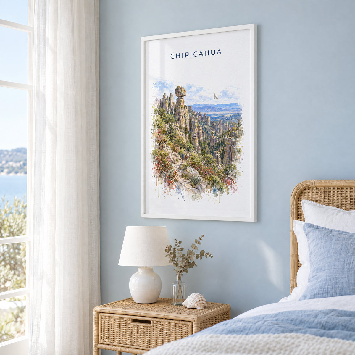 Chiricahua National Park watercolor print in a white frame on a pale blue wall beside a rattan bed in a coastal bedroom