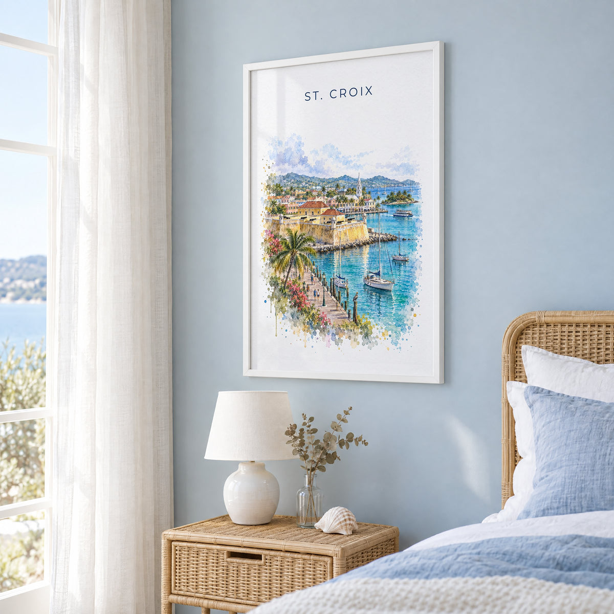 St. Croix watercolor print in a white frame on a pale blue wall beside a rattan bed in a coastal bedroom