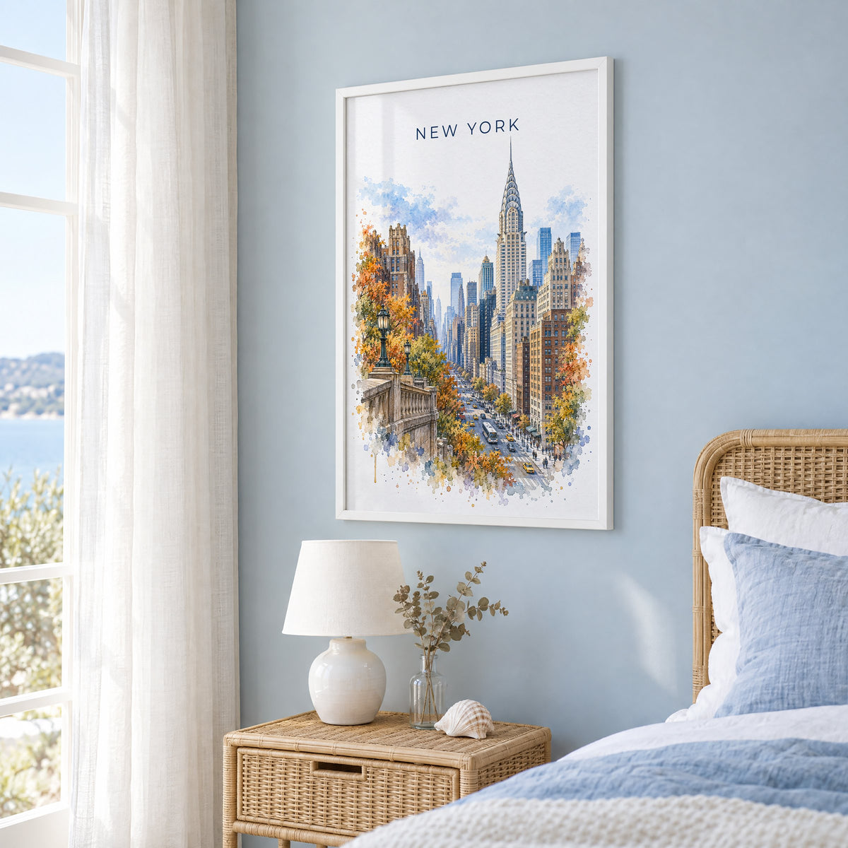 Chrysler Building watercolor print in a white frame on a pale blue wall beside a rattan bed in a coastal bedroom