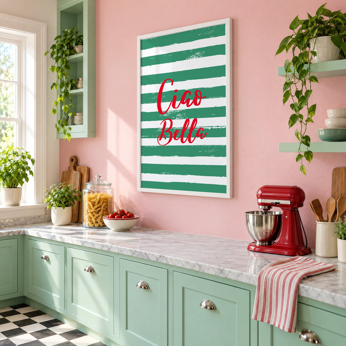 Ciao Bella red script on green stripes print in a white frame on a pink wall above mint green cabinets in a retro kitchen, seen at an angle