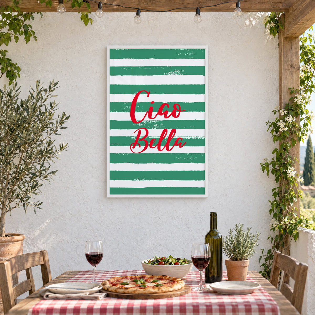 Ciao Bella red script on green stripes print in a white frame on a stucco wall above a checked-cloth table with pizza and red wine
