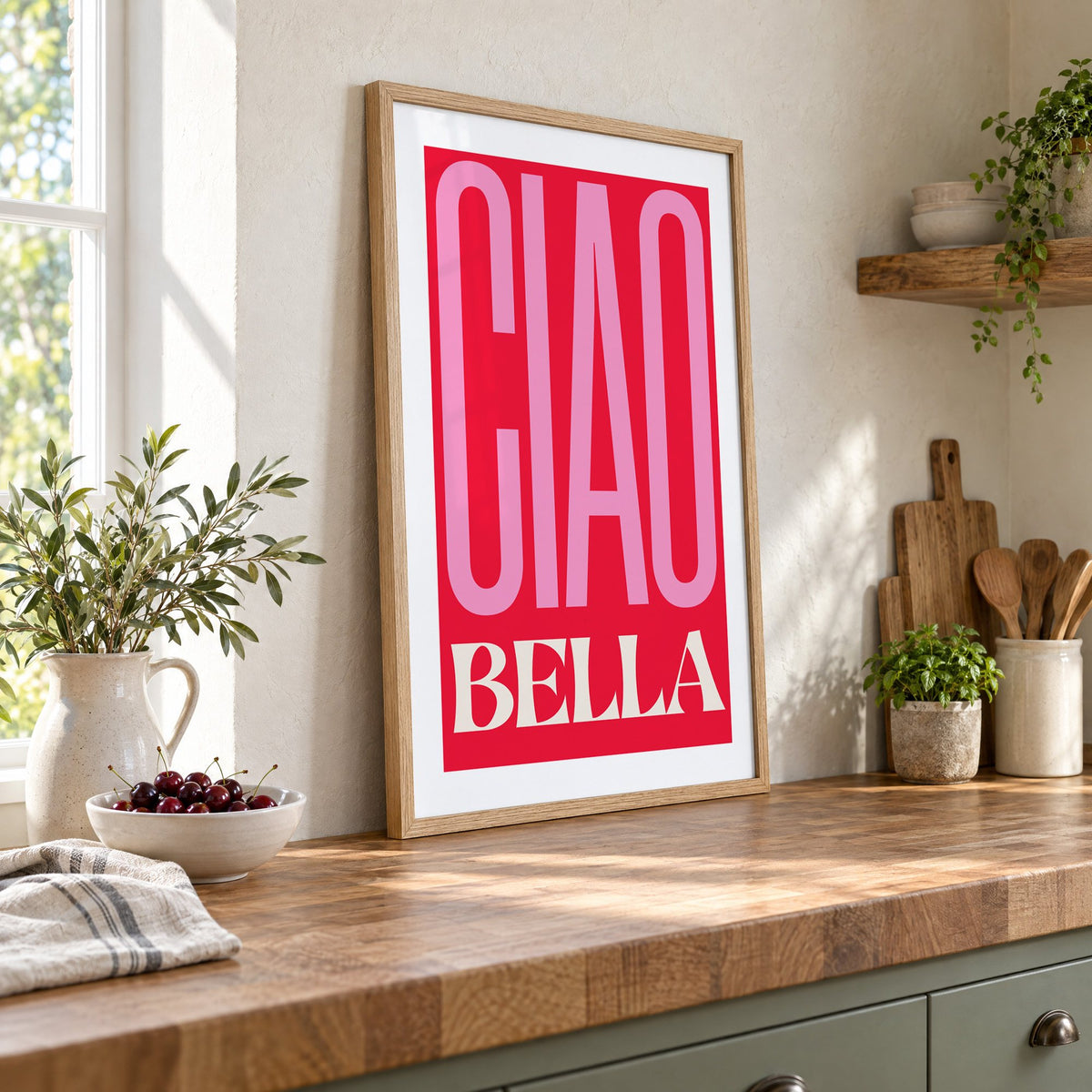 Ciao Bella pink and red type print in an oak frame leaning on a butcher block island beside a bowl of cherries