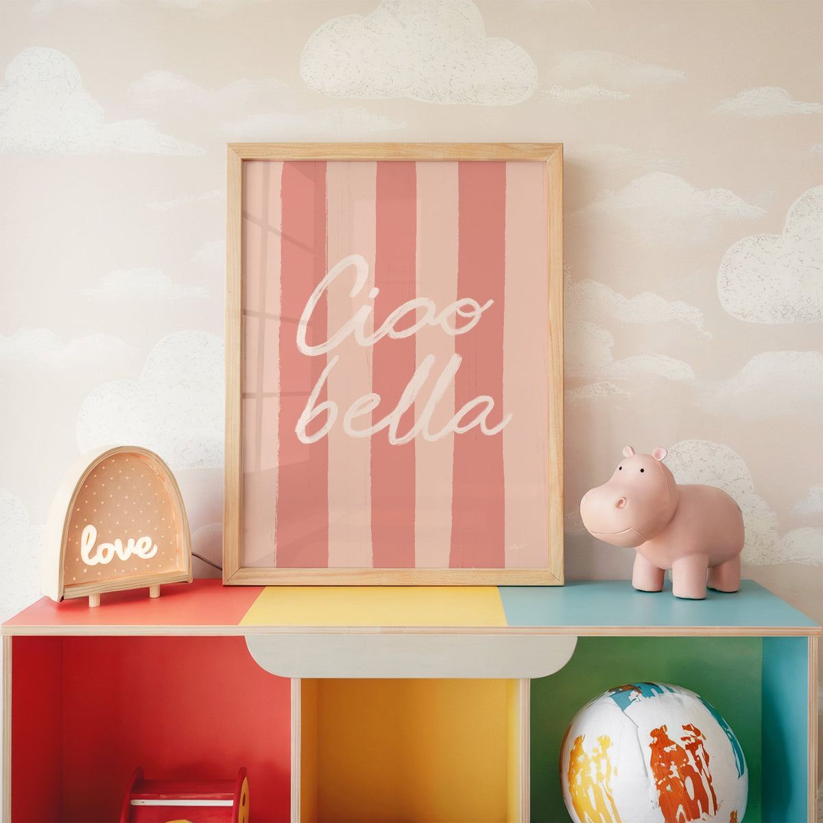 Ciao bella script on pink stripes nursery print in an oak frame on a rainbow toy shelf against cloud wallpaper