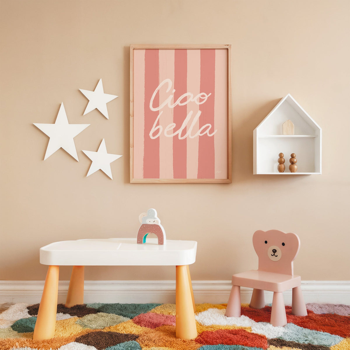 Ciao bella script on pink stripes nursery print in an oak frame on a peach wall above a kids table with wall stars