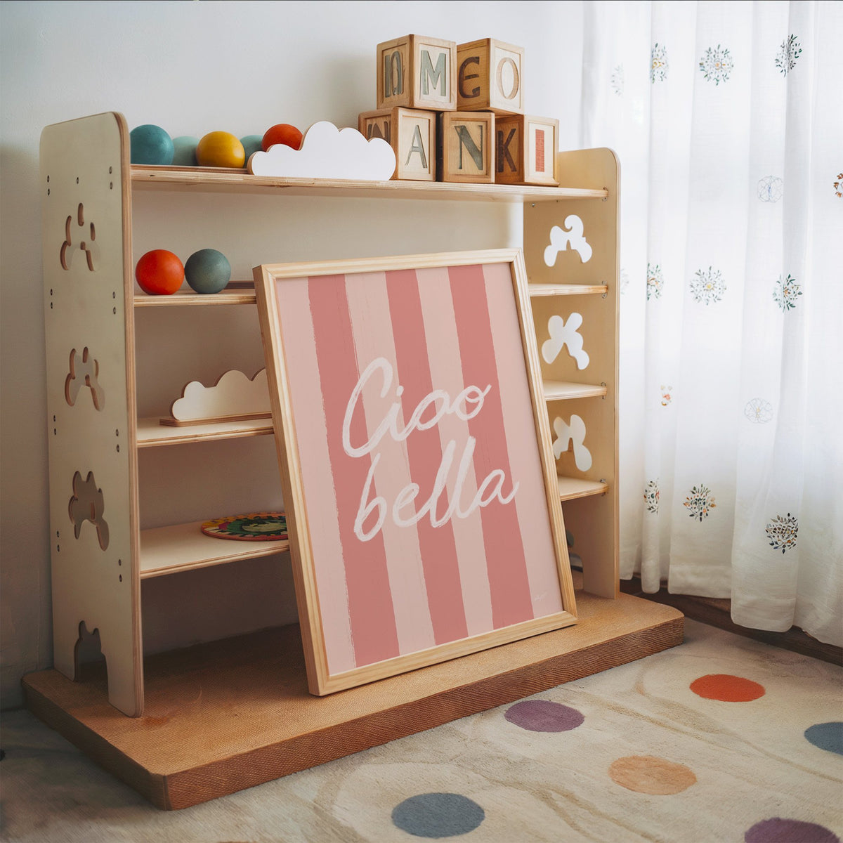 Ciao bella script on pink stripes nursery print in an oak frame leaning on a toy shelf with wooden letter blocks