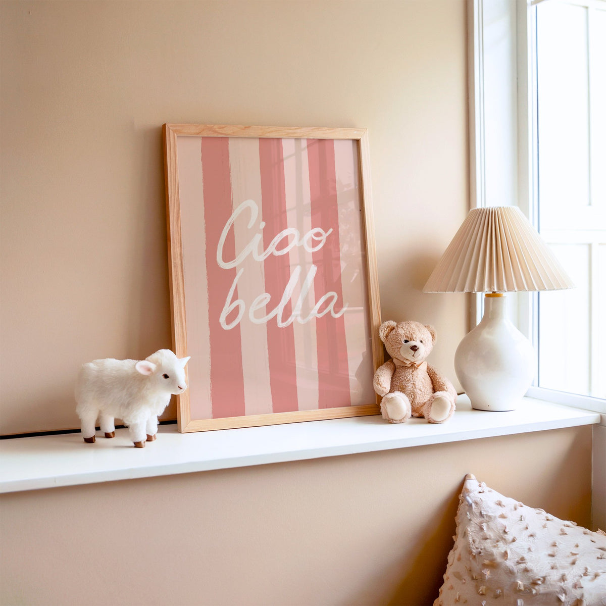 Ciao bella script on pink stripes nursery print in an oak frame on a window ledge with a toy lamb and teddy