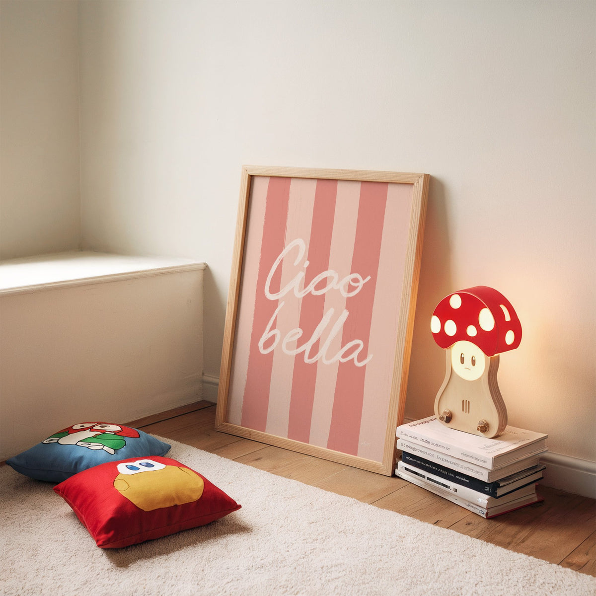 Ciao bella script on pink stripes nursery print in an oak frame leaning on a rug beside a mushroom lamp and floor cushions
