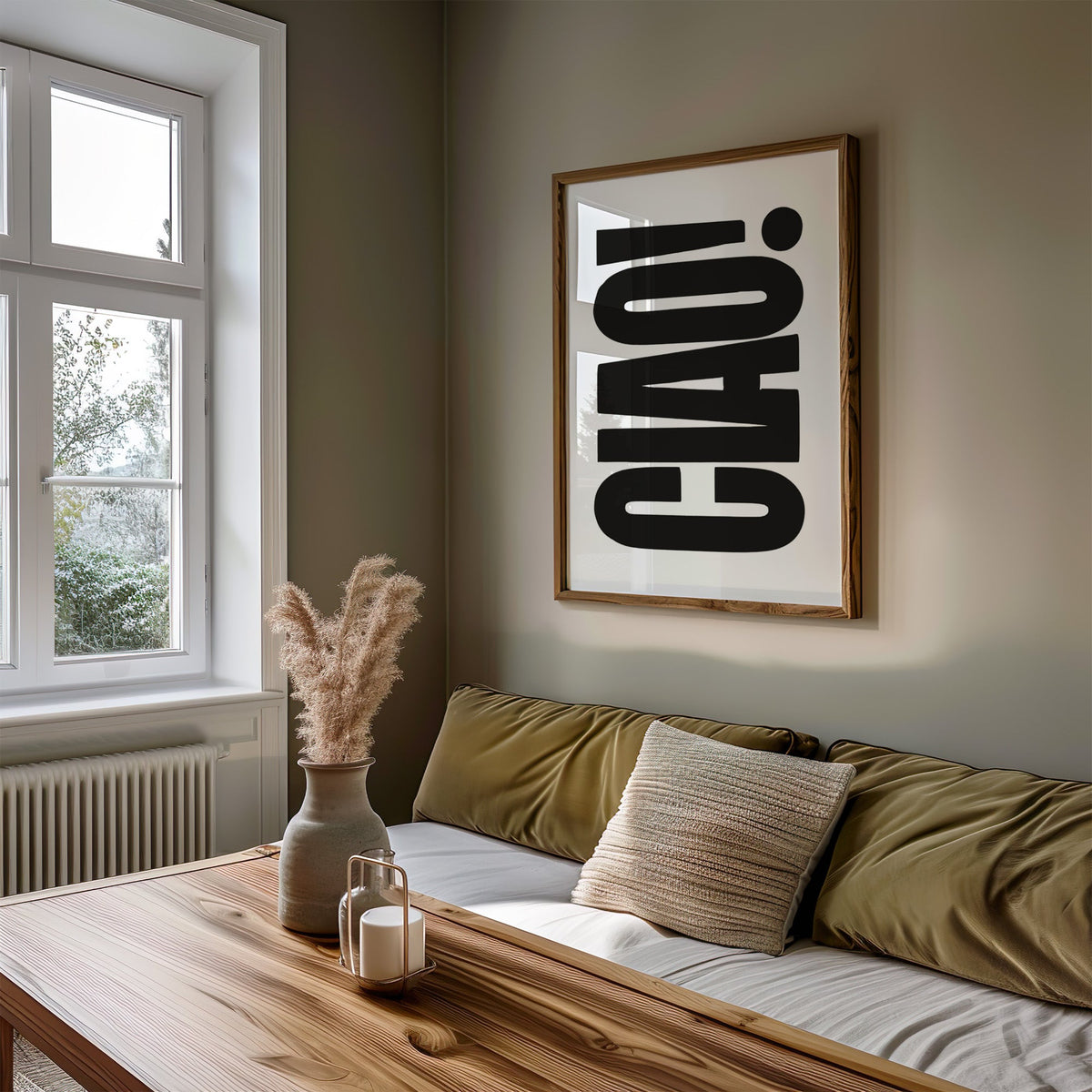 Rotated CIAO lettering on white print in a walnut frame above an olive daybed by a window