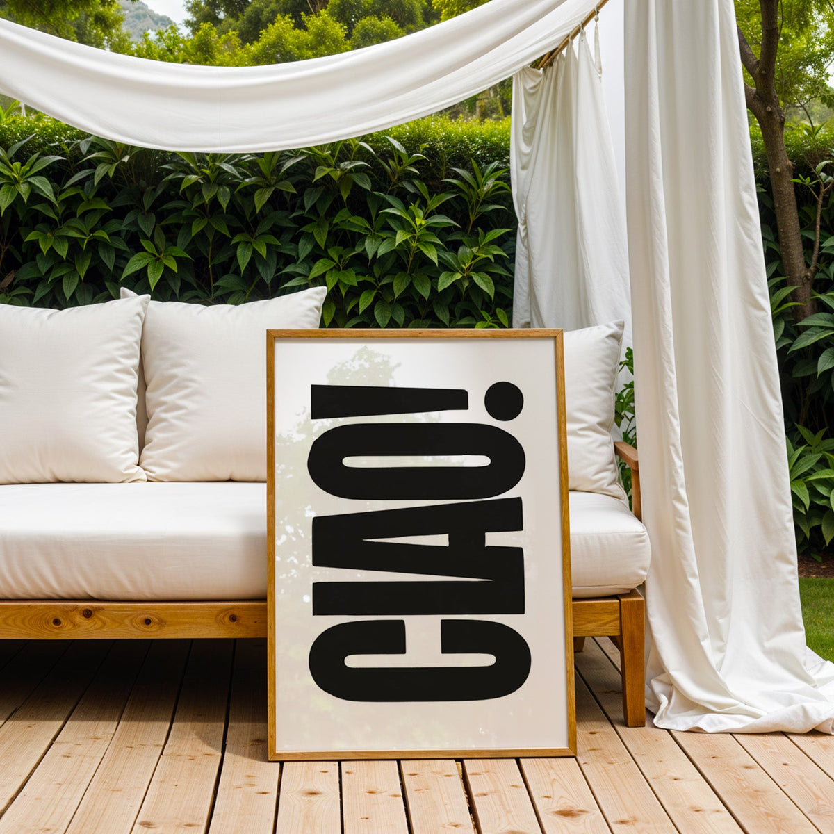 Rotated CIAO lettering on white print in an oak frame on an outdoor daybed under white drapes