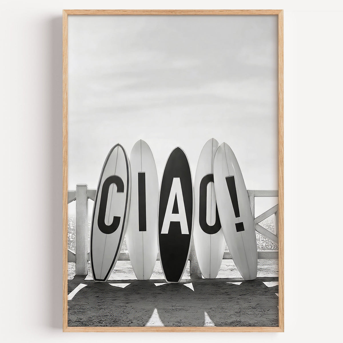 Five surfboards spelling CIAO by a beach fence print in a light oak frame on a plain white wall