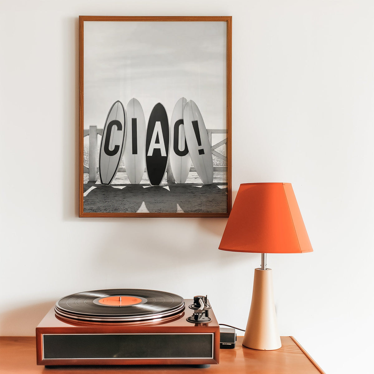 Five surfboards spelling CIAO by a beach fence print in a walnut frame above a record player and orange lamp
